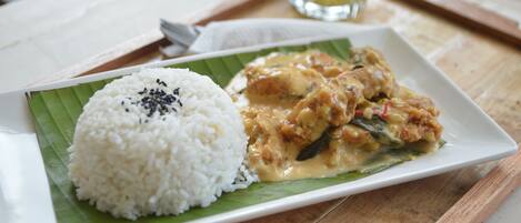 Prato de arroz branco com sementes de gergelim preto sobre folha de bananeira, acompanhado de um prato de curry em prato branco.
