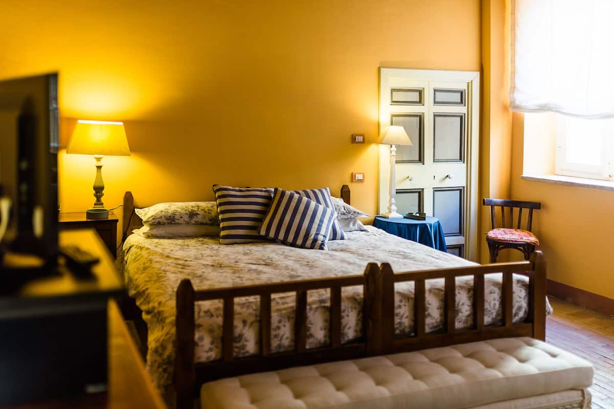 A bedroom with a bed, bedside lamps, a chair, a small table, and a door.