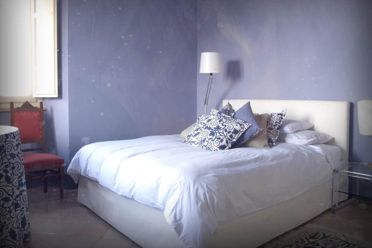 A bedroom with a bed, pillows, a chair, a table, and a lamp.