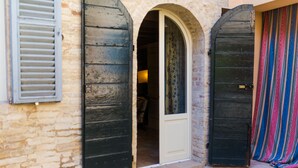 A stone building with two large wooden doors and a small arched entrance. - Palazzo Romani Adami (Fermo)