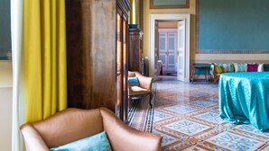 A room with a patterned floor, a wooden cabinet, a leather armchair, and a table with a blue tablecloth. - Palazzo Romani Adami (Fermo)