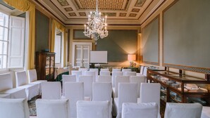 A formal room with rows of white chairs, a chandelier, and a large table with plates. - Palazzo Romani Adami (Fermo)
