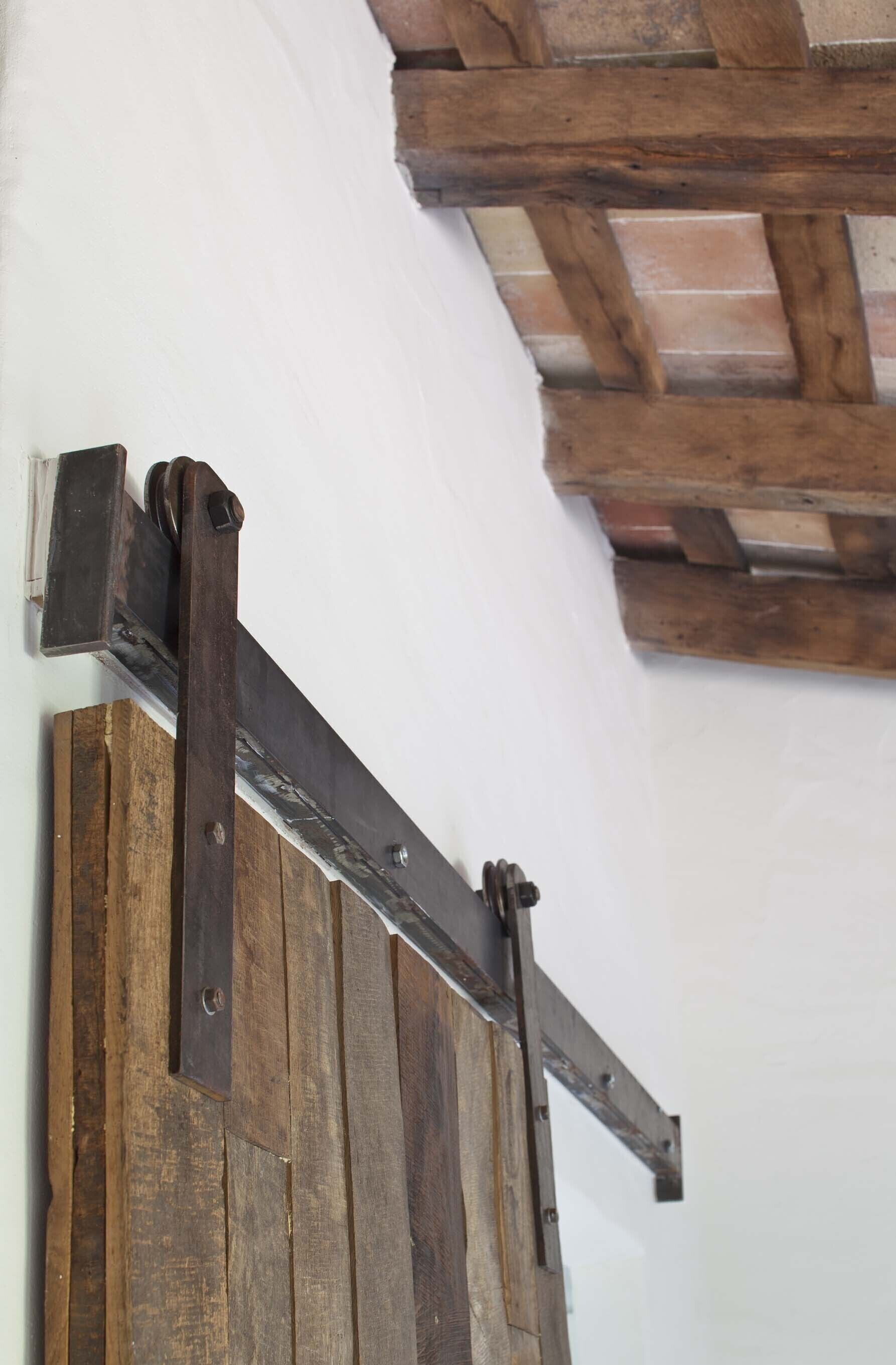 A wooden sliding door with metal hardware, set against a white wall and a wooden ceiling beam.
