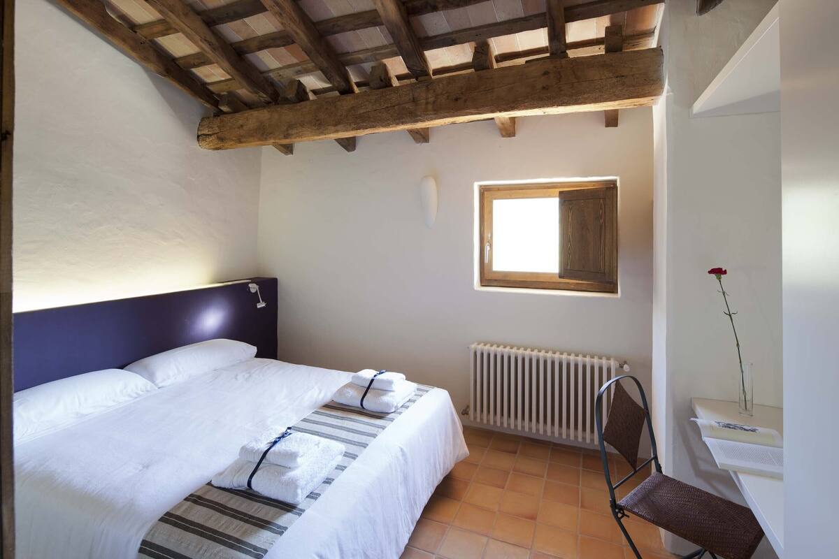 A bedroom with a bed, a window, a radiator, and a chair.