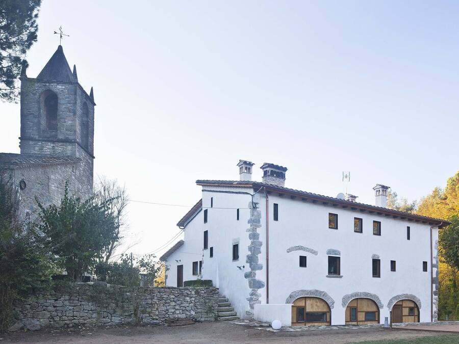A white building with a stone tower, arched doorways, and a staircase leading to a wooden door.