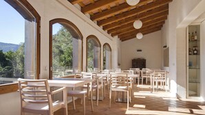 A spacious outdoor dining area with multiple tables and chairs, large windows offering views of the surrounding landscape, and a wooden ceiling structure. - La Rectoria De Sant Miquel De Pineda (Sant Feliu de Pallerols)