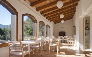Un amplio espacio de comedor al aire libre con múltiples mesas y sillas, grandes ventanales que ofrecen vistas del paisaje circundante y una estructura de techo de madera.