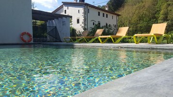 Una piscina con agua cristalina, rodeada por un solárium de hormigón. Hay dos sillas reclinables amarillas y un flotador anclado a la pared de la piscina.