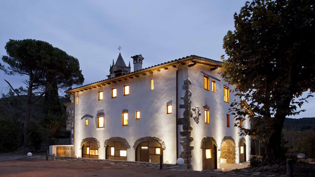 A historic building with multiple arched doorways and a tower with a spire. - La Rectoria De Sant Miquel De Pineda (Sant Feliu de Pallerols)