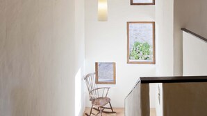 A staircase leading to a room with a wooden rocking chair, two framed artworks, and a view of greenery outside. - La Rectoria De Sant Miquel De Pineda (Sant Feliu de Pallerols)