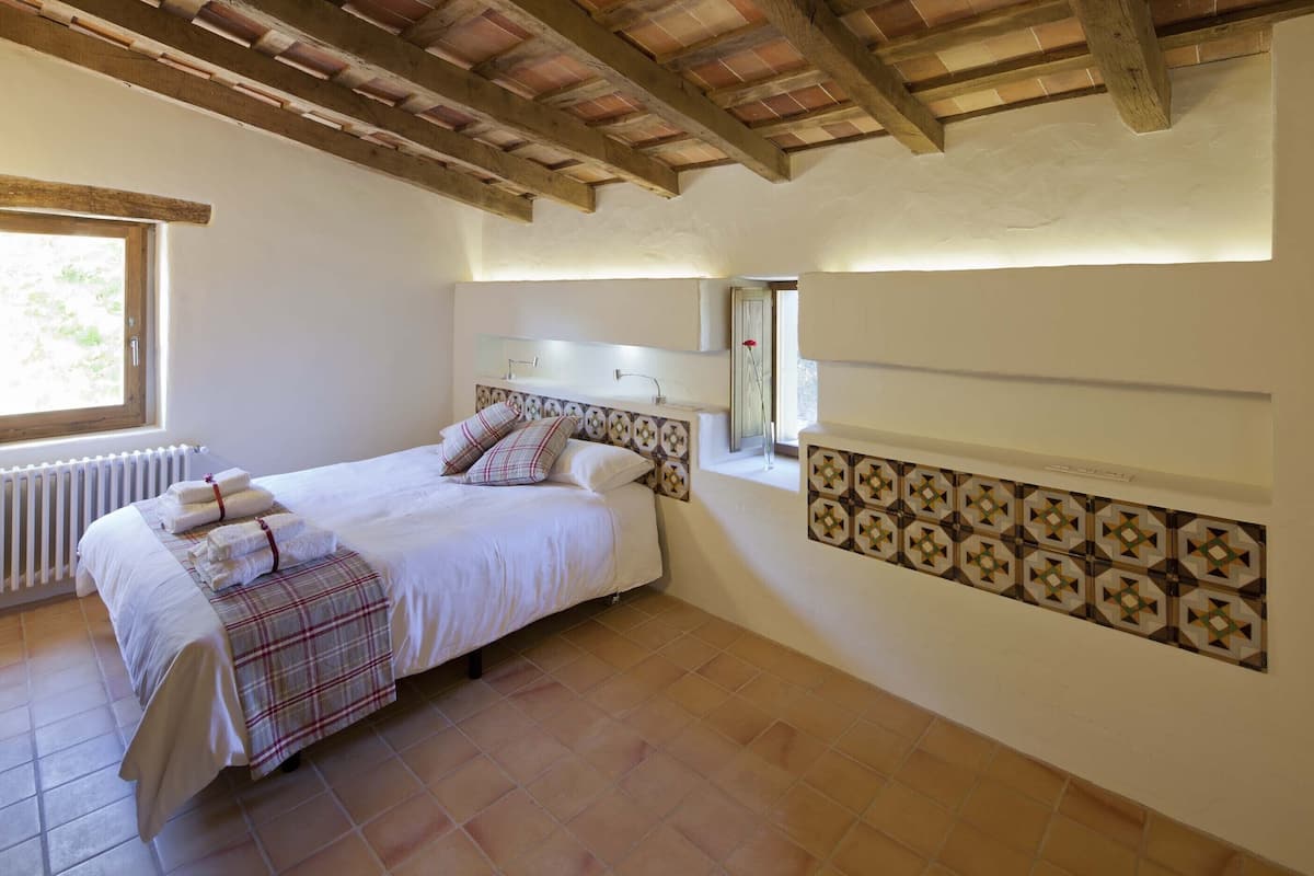 A bedroom with a bed, a window, a radiator, and a decorative wall panel.