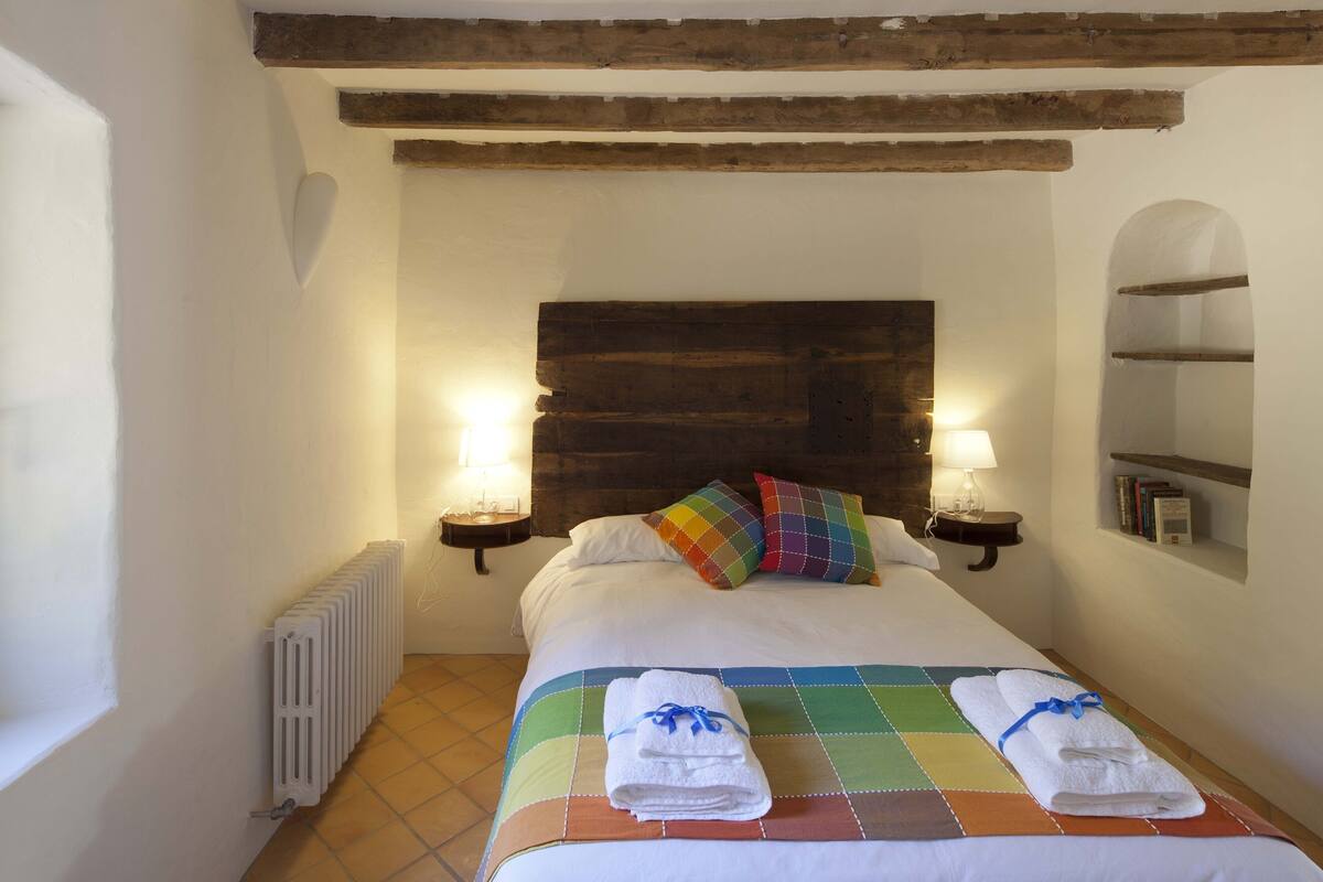 A neatly made bed with a colorful quilt, two bedside lamps, and a wooden headboard.