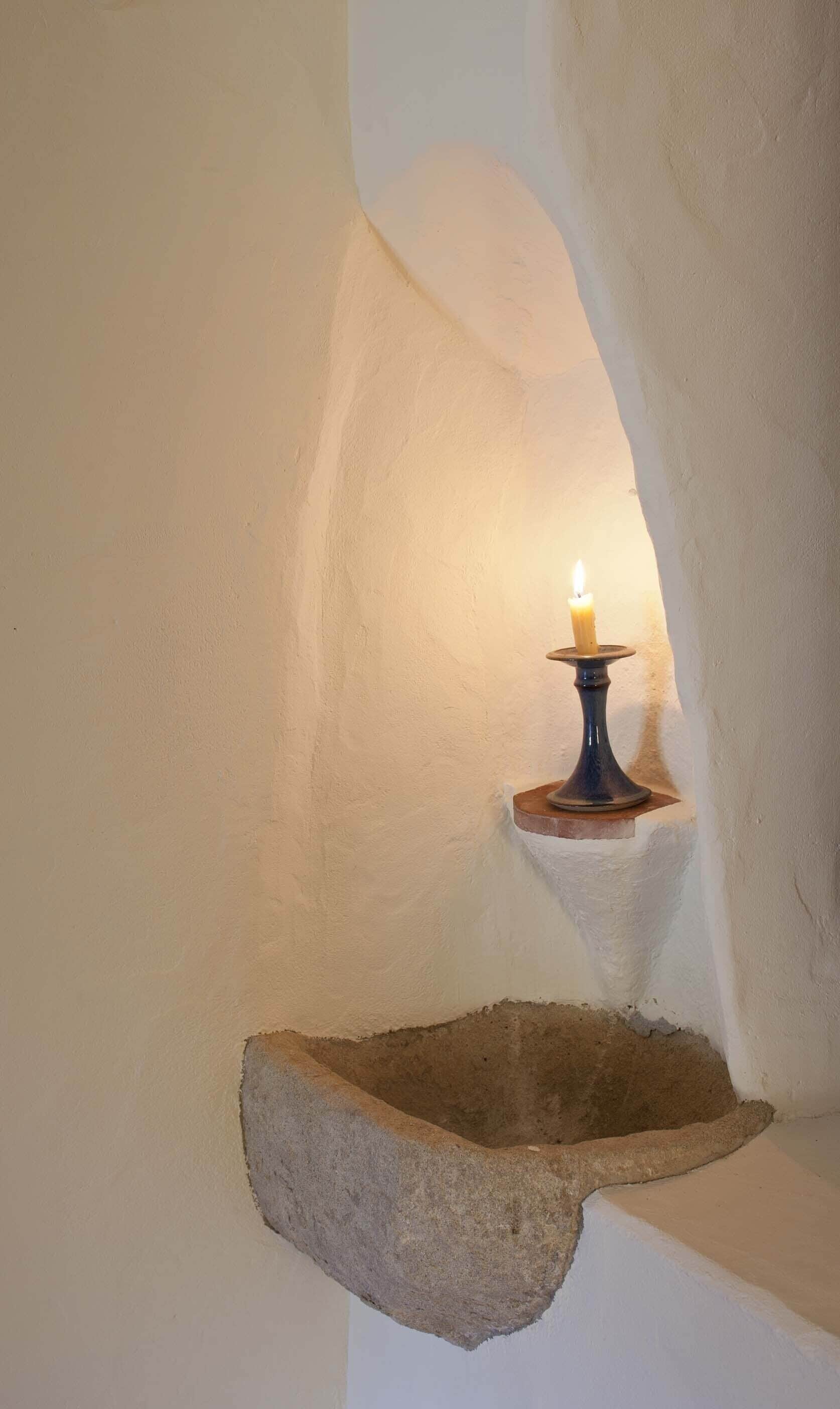 A candlelit alcove with a stone shelf and a candle on a blue stand.