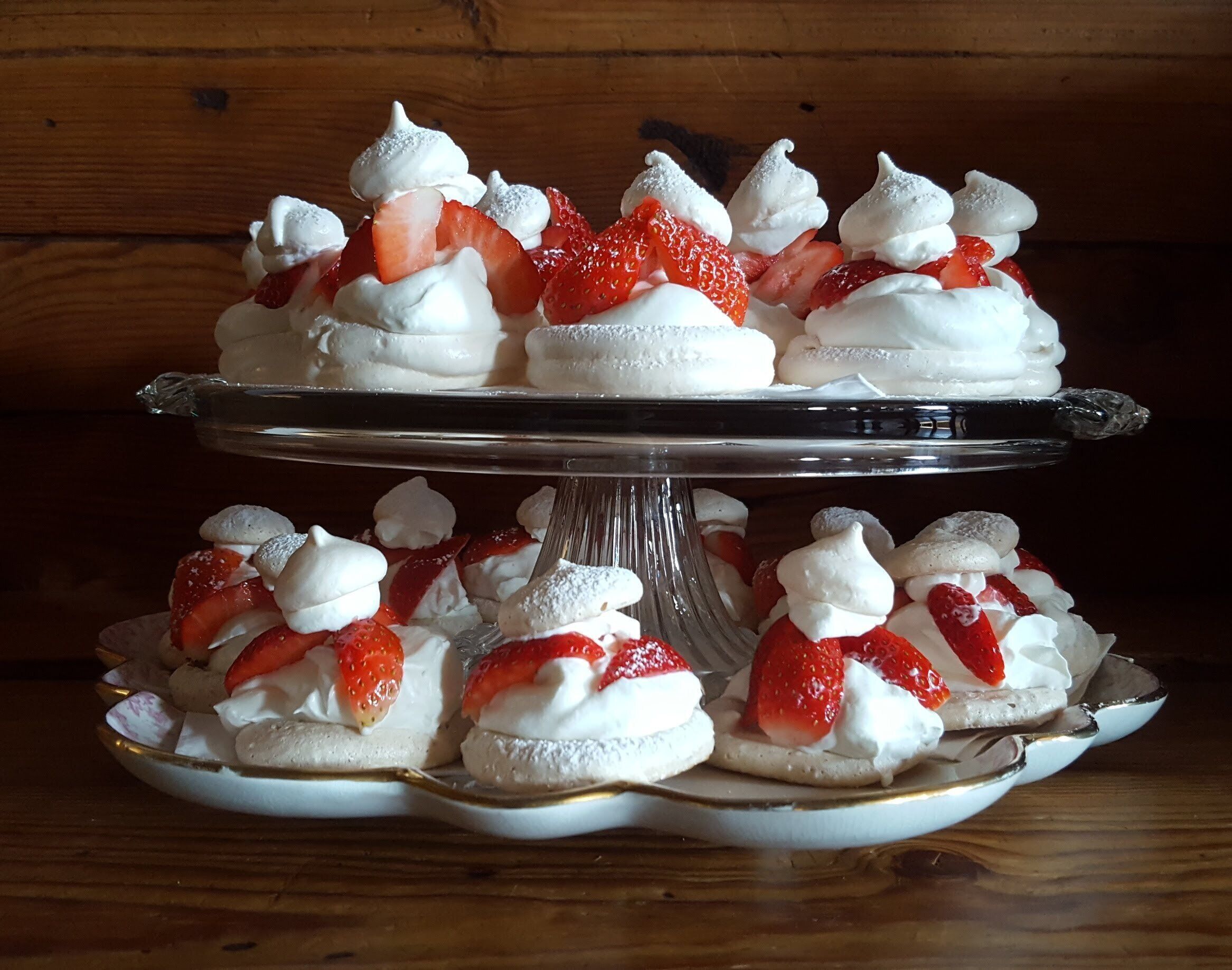 Une présentation de desserts comprenant des pavlovas surmontées de meringue et des fraises, le tout disposé sur un présentoir en verre.