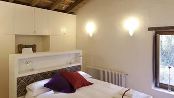 Un dormitorio con cama, paredes blancas, techo de madera, radiador y ventana con vistas.