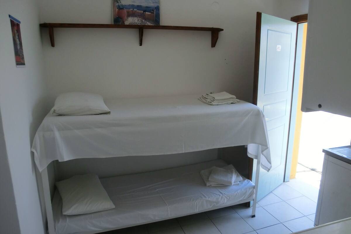 Habitación individual con una cama nido, un cuadro en la pared y una puerta que da a un balcón.