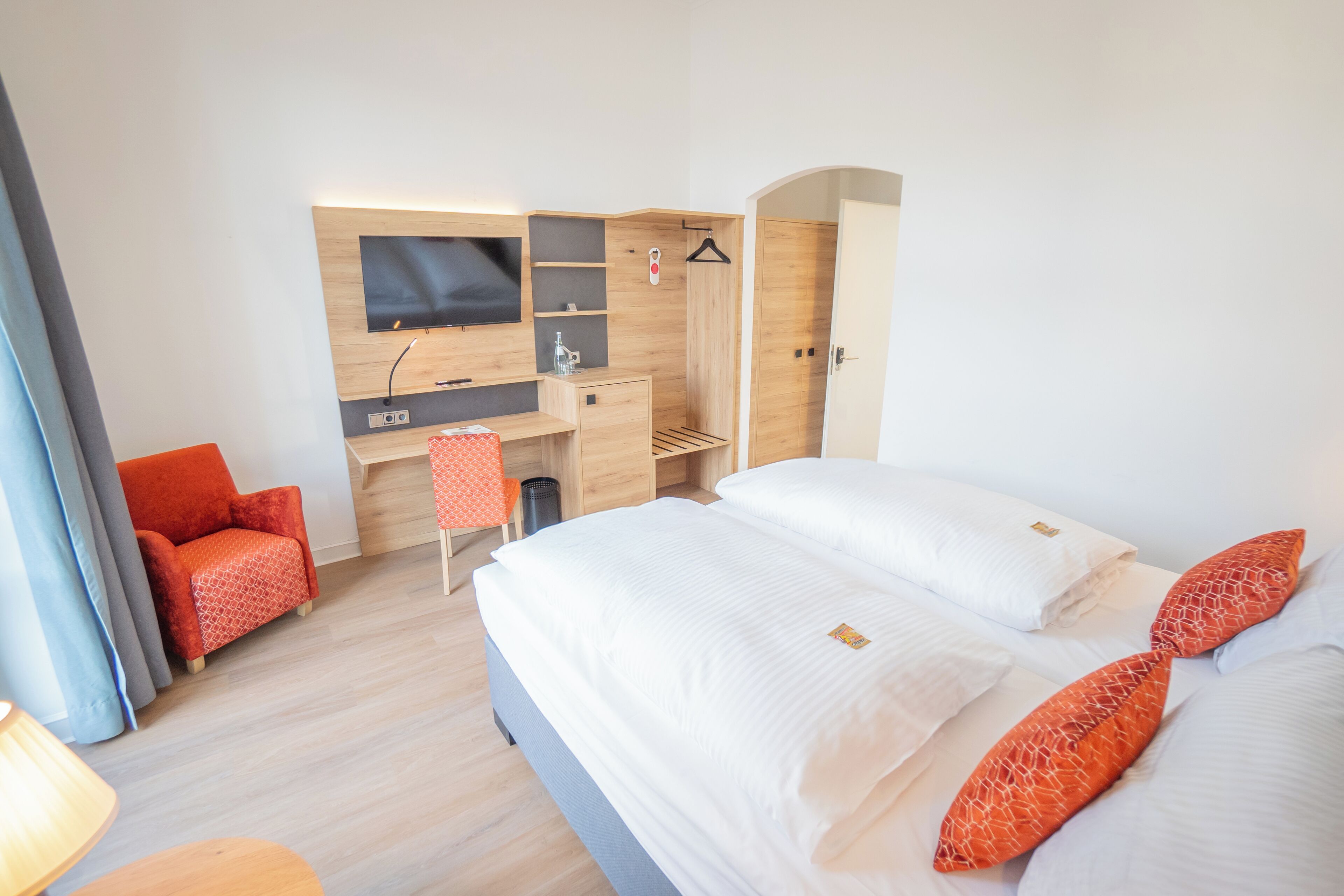 A modern hotel room with a large bed, a desk, a TV, and a shower area.