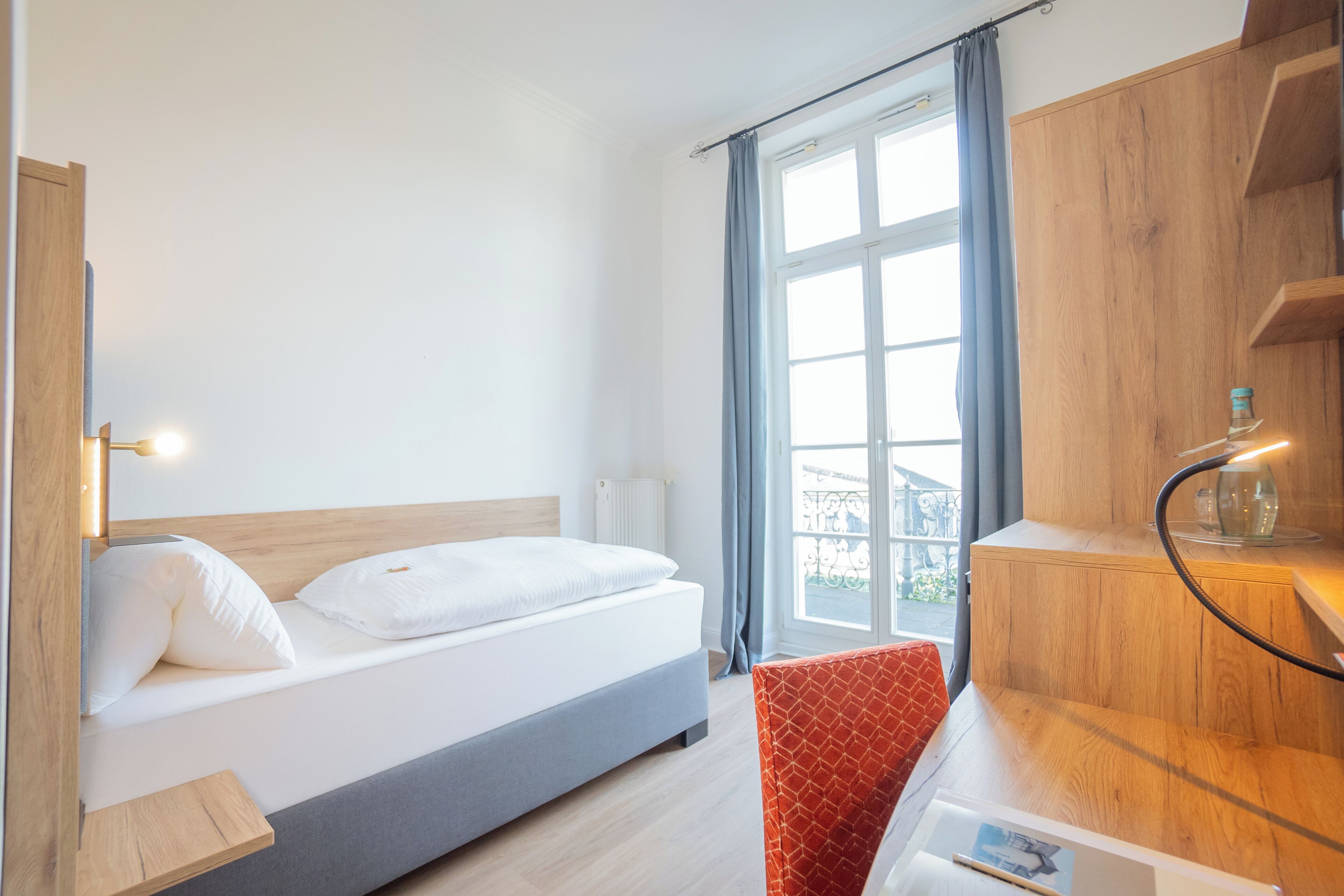 Habitación de hotel con cama, escritorio, silla, ventana con cortinas y un armario de madera.