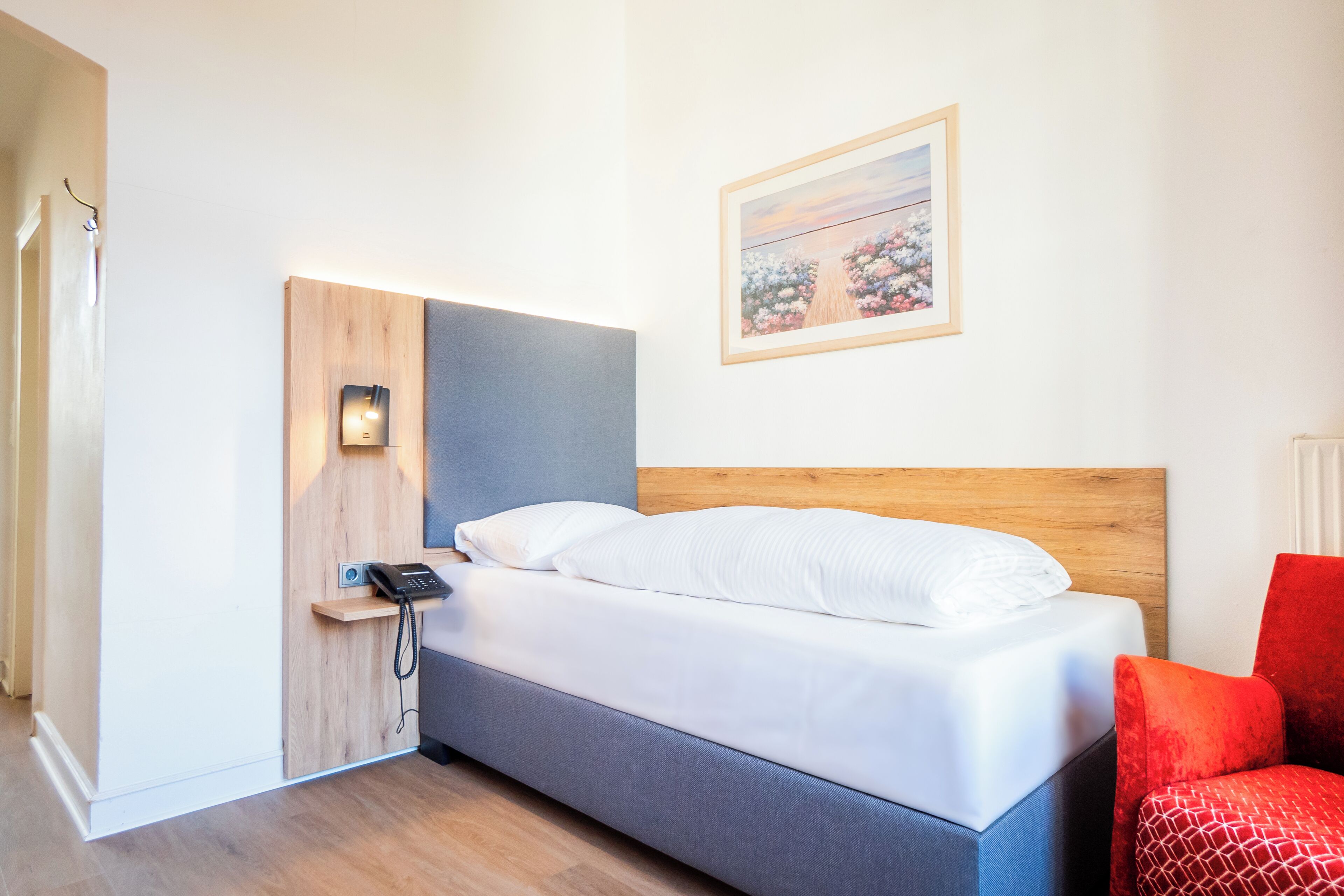 A bedroom with a bed, a phone, a red chair, and a painting on the wall.