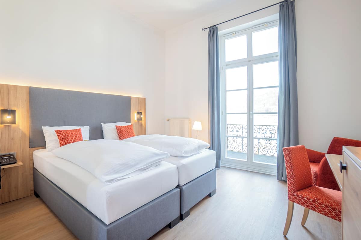 A modern hotel room with a large bed, bedside tables, a desk, and a window with curtains.