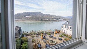 A riverside view from a window overlooking a riverside patio with outdoor seating and a small fountain.