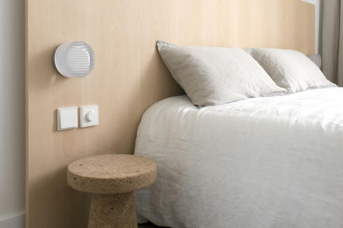 Un dormitorio con cabecera de madera, un taburete redondo y una cama con ropa de cama blanca.