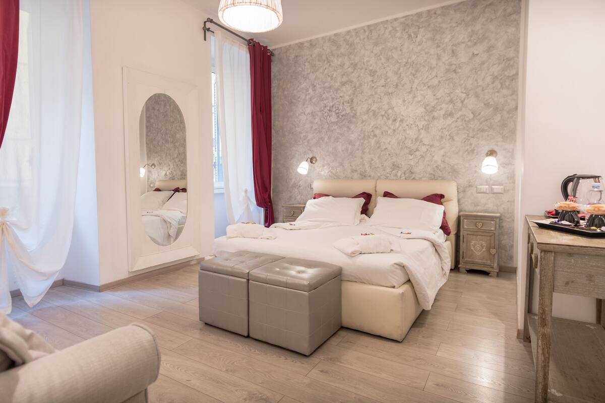 A modern bedroom with a large bed, a bedside table, a nightstand, and a small table with a kettle and cups.