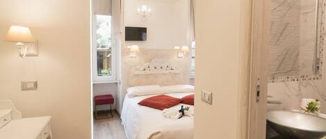 Una habitación de hotel con cama, mesita de noche, lámpara y baño con lavamanos y espejo.