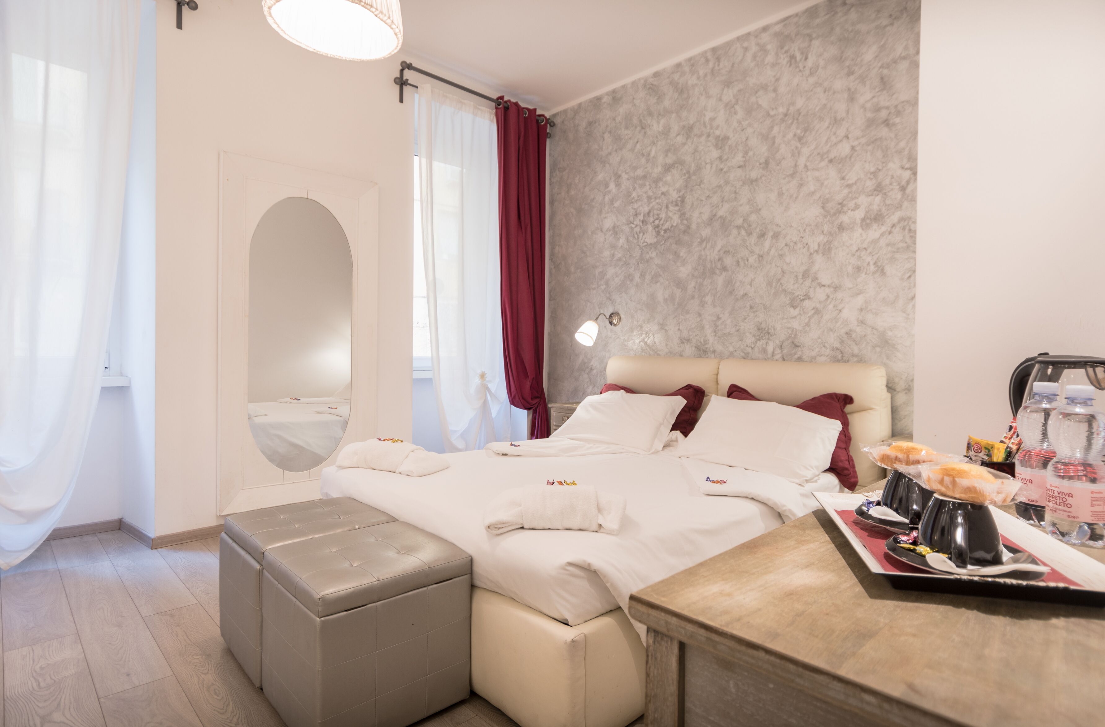 Ein Hotelzimmer mit einem Bett, einem Nachttisch mit einem Tablett Essen, einem Spiegel und einem Fenster mit Vorhängen.