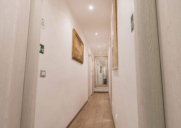 A hallway with wooden floors, white walls, and a framed picture on the wall. - Your Vatican Suite (Rome)