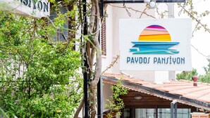 A sign with a colorful design and the text "PAYDOS PANSIYON" against a backdrop of a building and greenery. - Paydos Pansiyon (Kas)