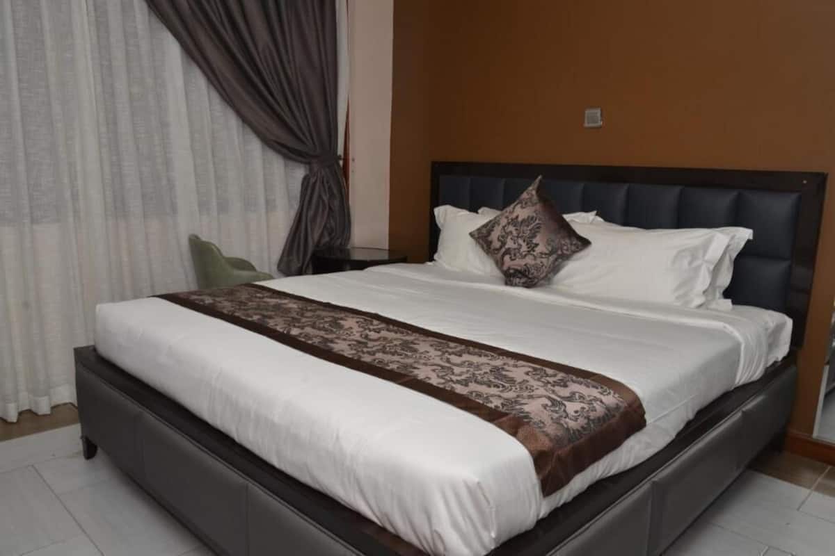 A bed with a dark headboard, white bedding, and a brown decorative throw.