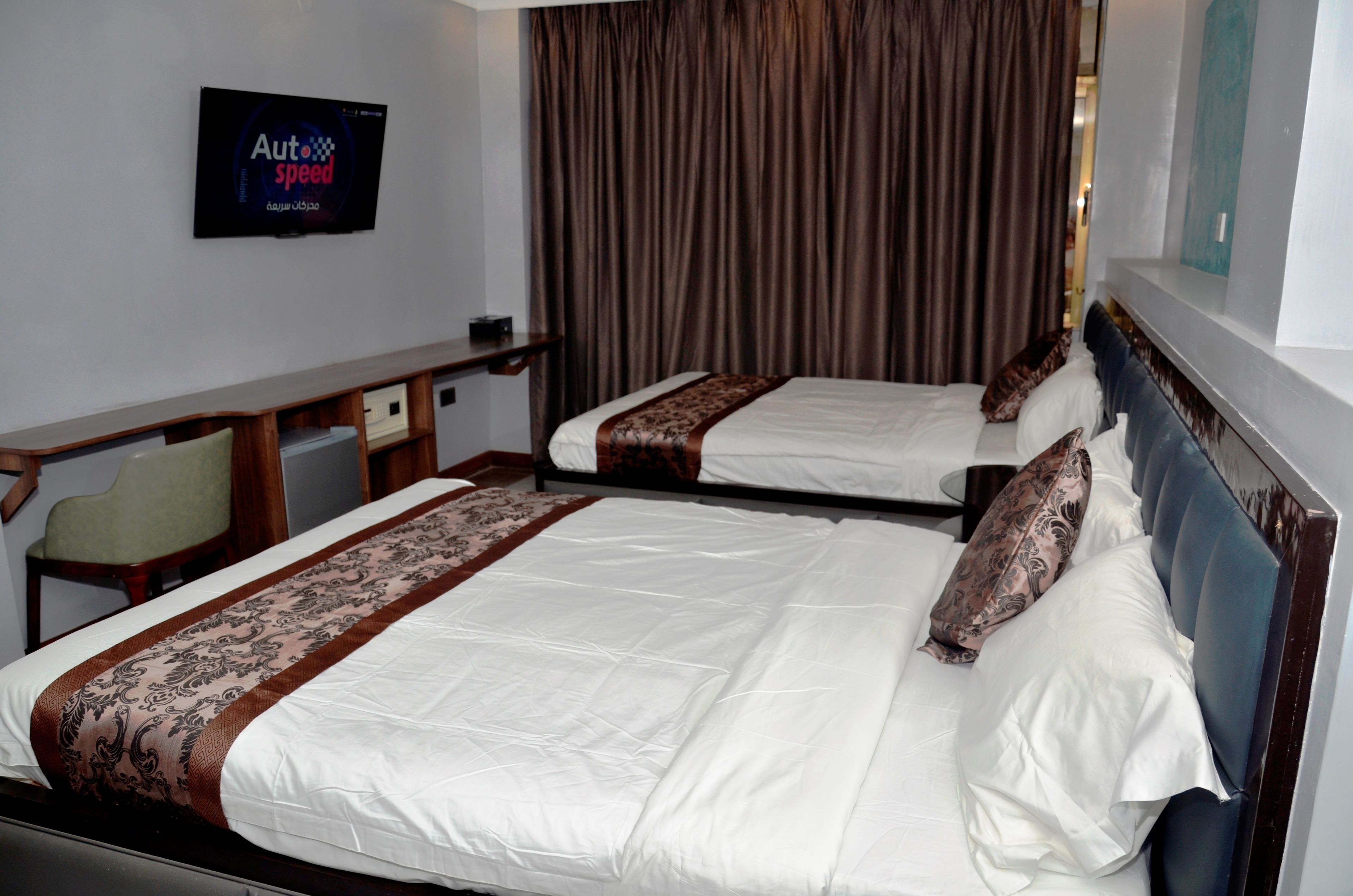Habitación de hotel con dos camas, un escritorio, una silla y un televisor que muestra 'Auto speed'.