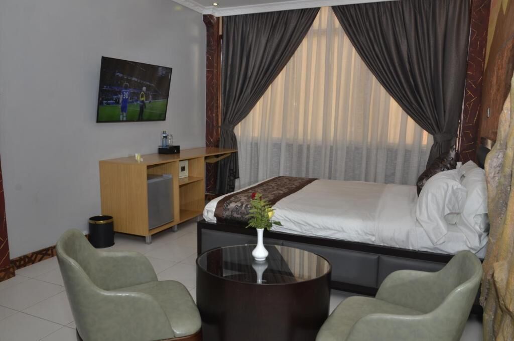 Una habitación de hotel con cama, escritorio, dos sillas, televisor en la pared y ventana con cortinas.