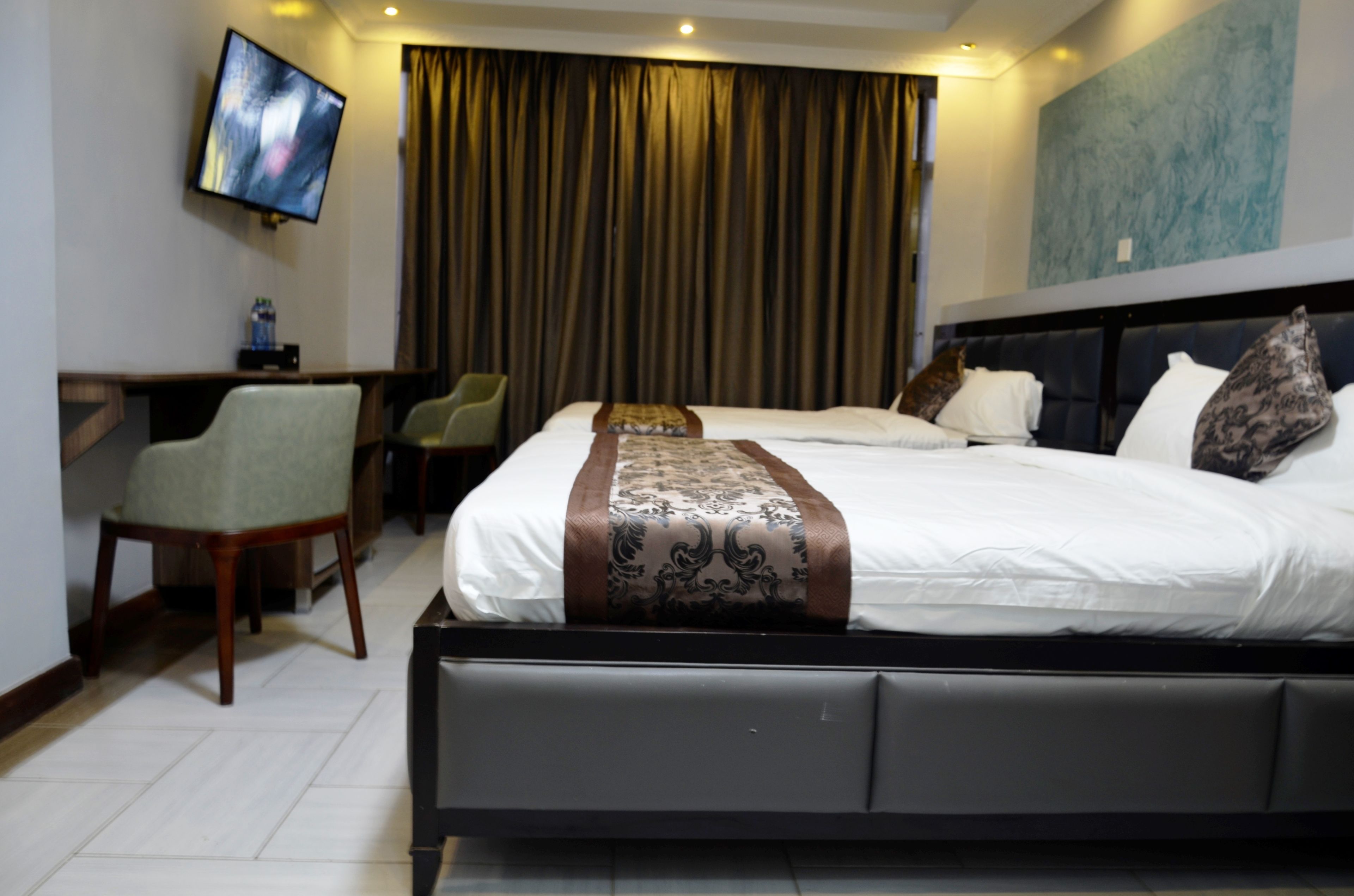 Habitación de hotel con una cama grande, un escritorio con silla, televisión y una cortina.