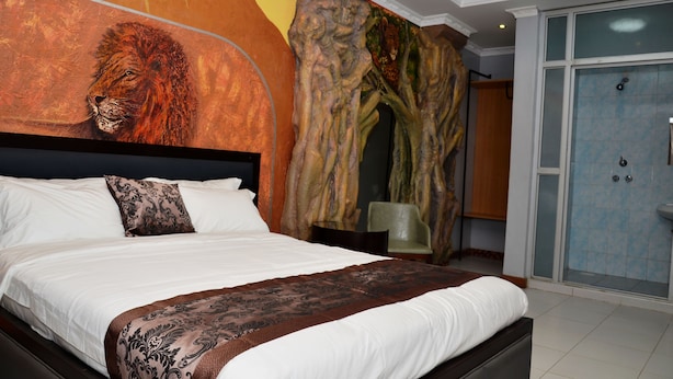 A bedroom with a large bed, a mural on the wall, and a shower area. - Lagos Hotel (Nairobi)