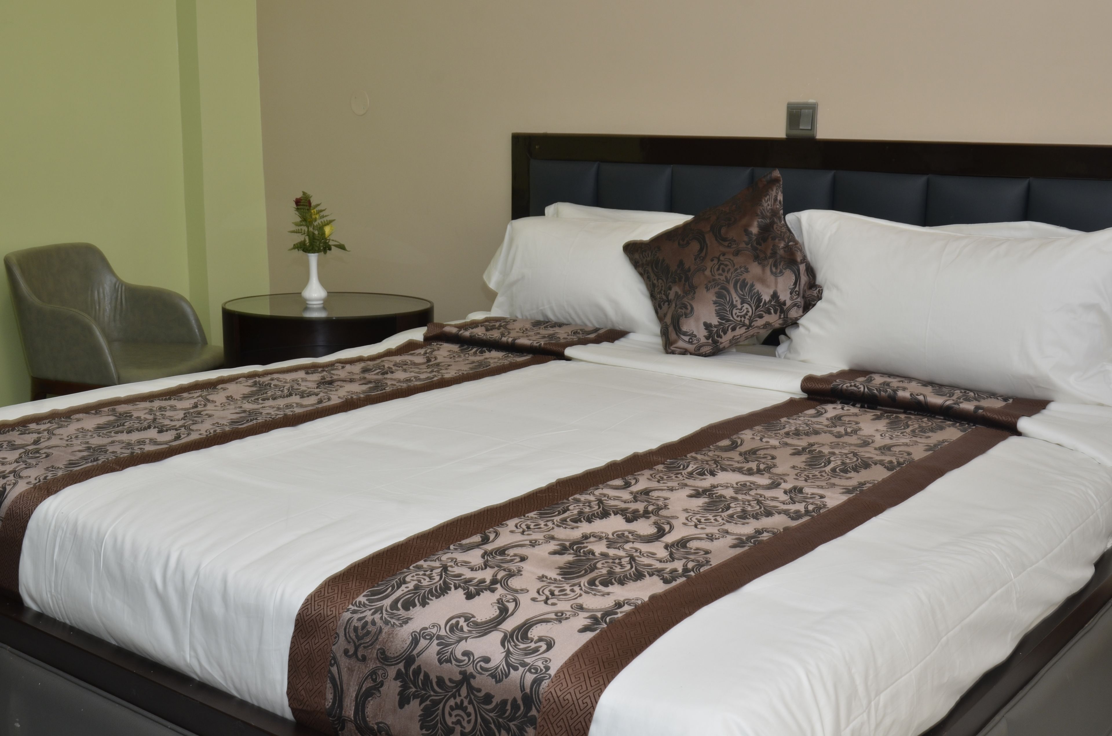 A neatly made bed with a patterned bedspread, a decorative pillow, and a vase of flowers on a bedside table.