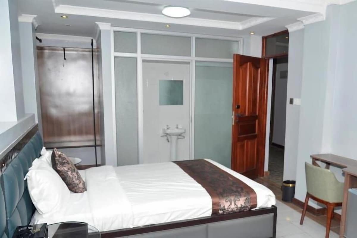 Une chambre d’hôtel équipée d’un lit, d’un bureau, d’une télévision et d’une salle de bain avec un miroir et un lavabo.