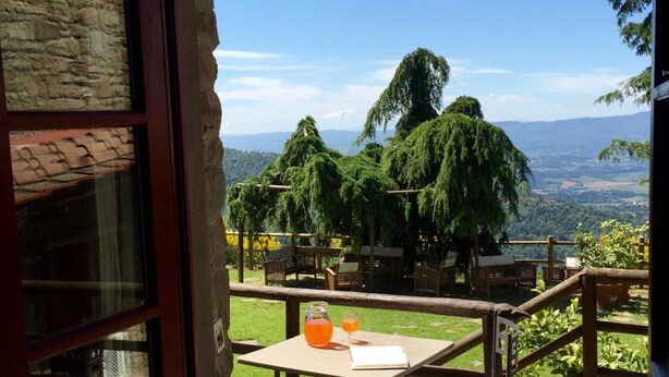 An open door leading to a patio with a table, chairs, and a view of a green landscape with trees and distant hills. - Borgo La Capraia (Castelfranco Piandisco)