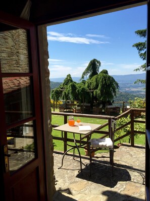 An open door leading to a patio with a table, chairs, and a view of a green landscape with trees and distant hills. - Borgo La Capraia (Castelfranco Piandisco)