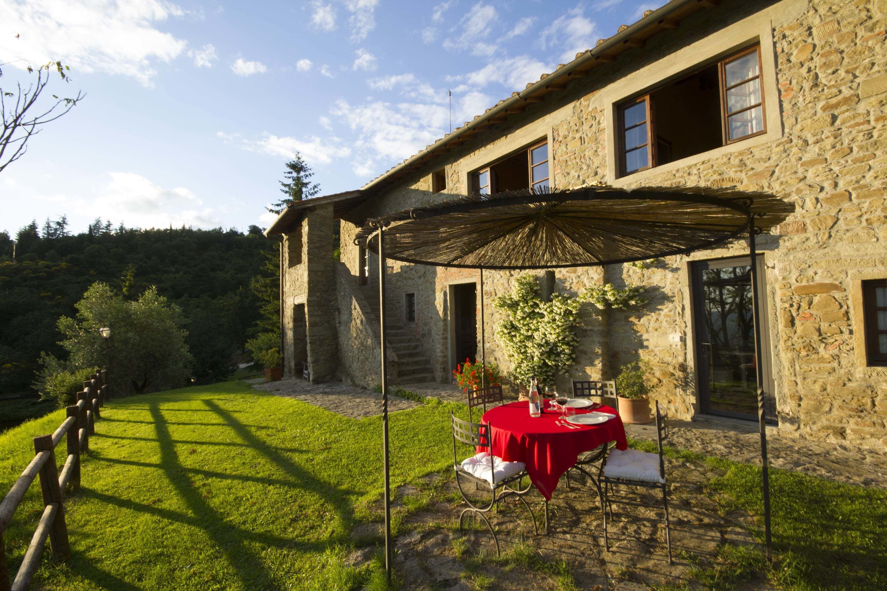 A stone building with a covered outdoor dining area, a wooden fence, and a grassy lawn.