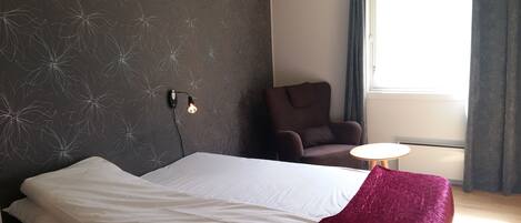A bedroom with a bed, a chair, a table, and a window with curtains.