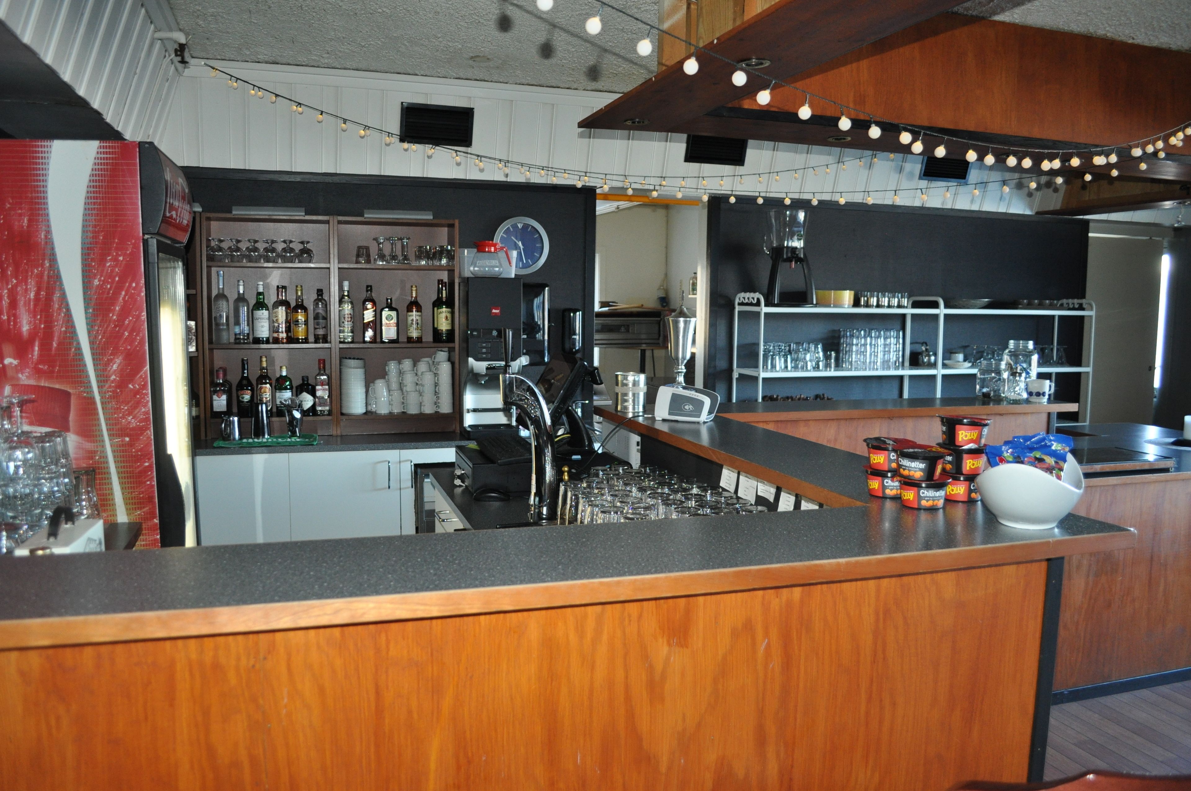 Un espace bar avec un comptoir, des étagères remplies de bouteilles et de verres, et une horloge.
