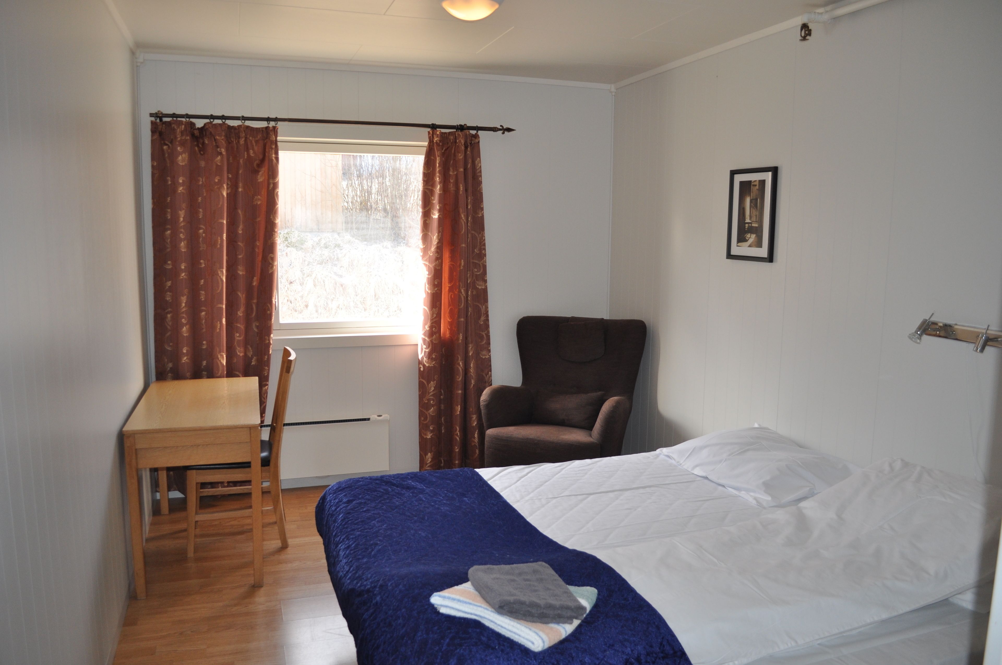 A room with a bed, a chair, a table, and a window with curtains.