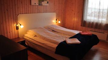 A bed with a headboard labeled "TRENOR DÖRER," two bedside lamps, a window with a sheer curtain, and a wooden floor.