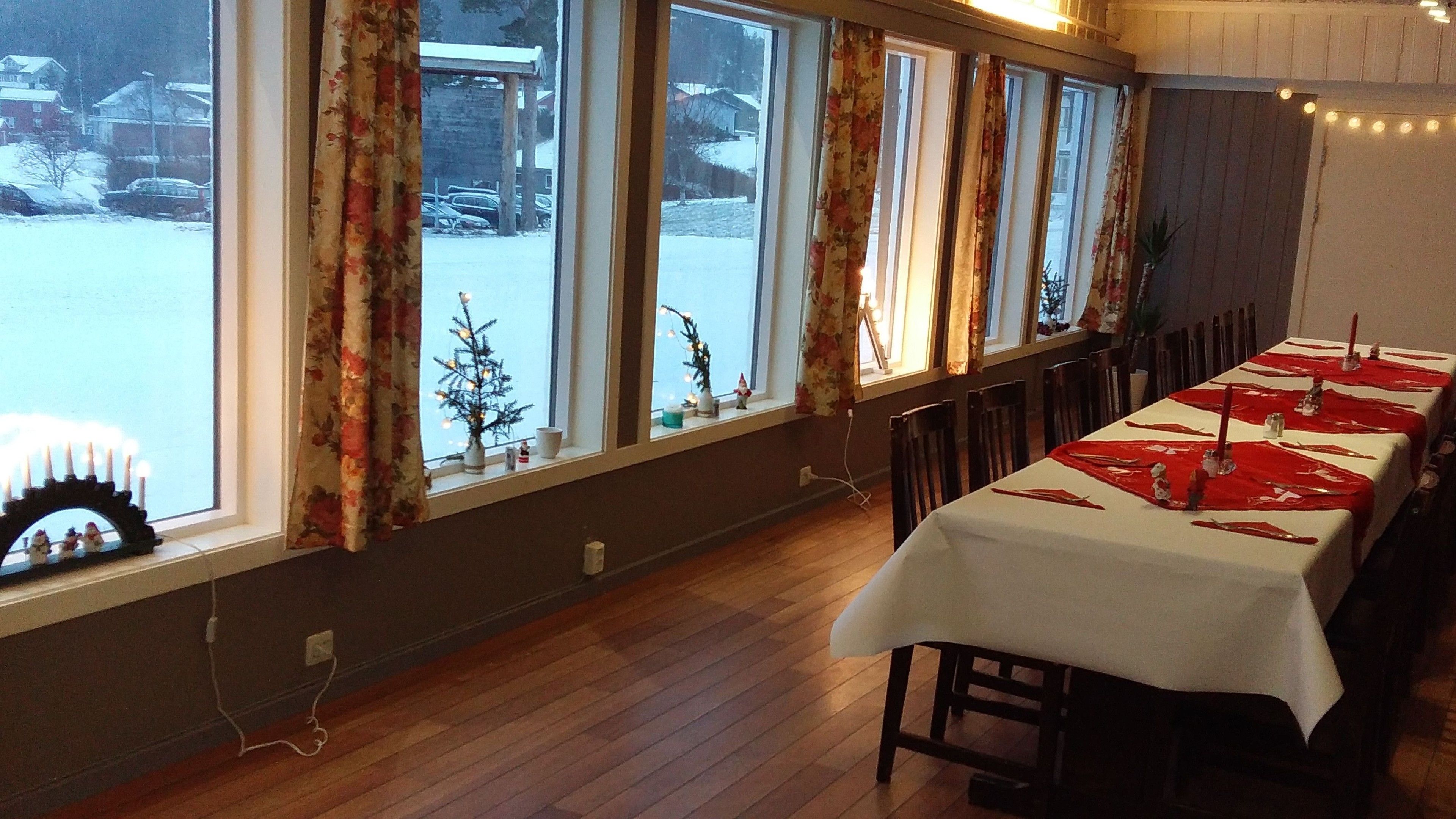 Un comedor con una mesa larga dispuesta para una comida, ventanas amplias con cortinas y vistas a un paisaje nevado.