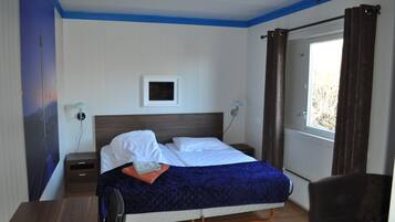 Una cama bien hecha con sábanas blancas, una colcha azul acolchada y una mesita de noche con una lámpara.