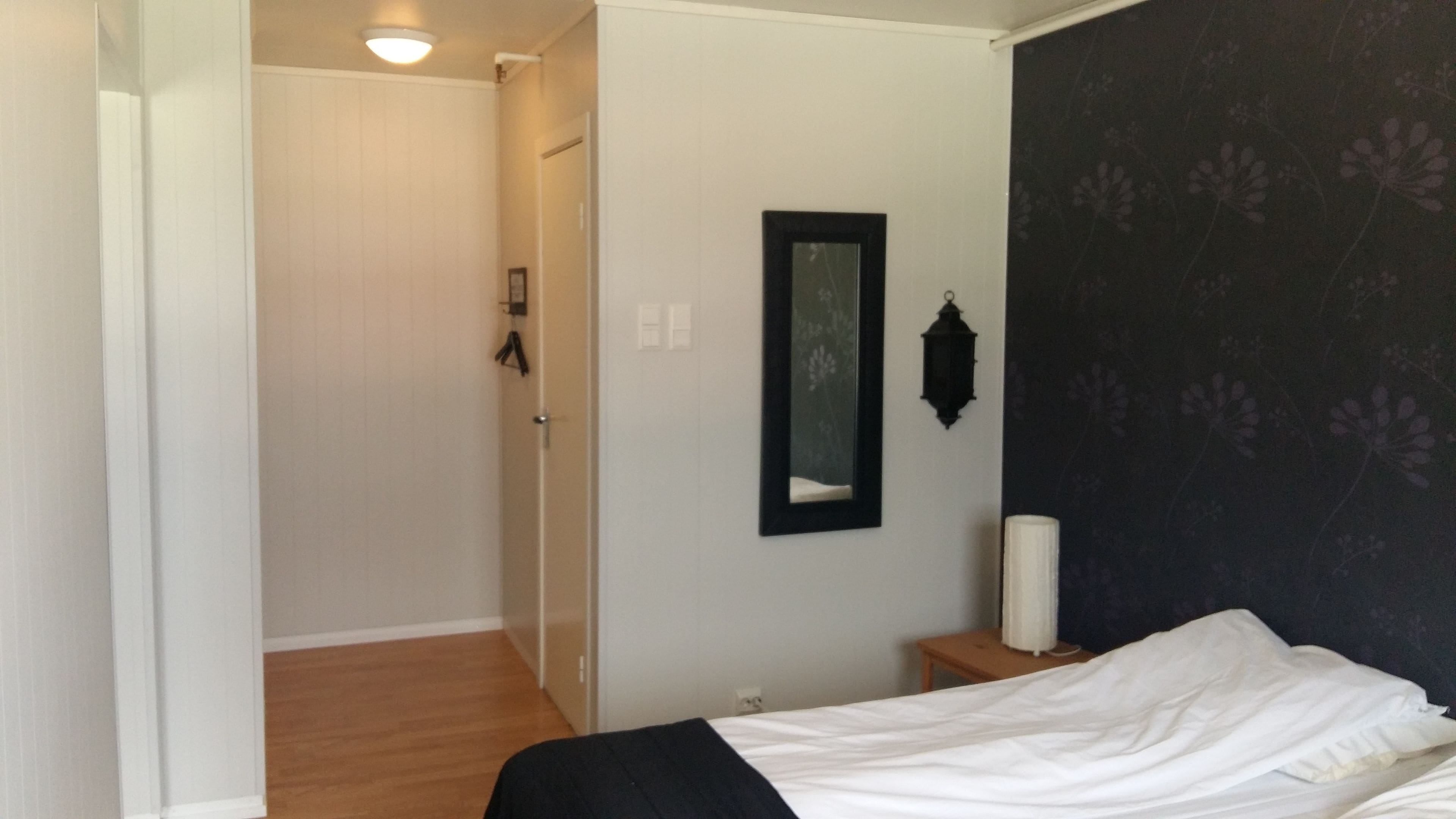 A bedroom with a bed, a nightstand, a mirror, and a wall with a floral pattern.