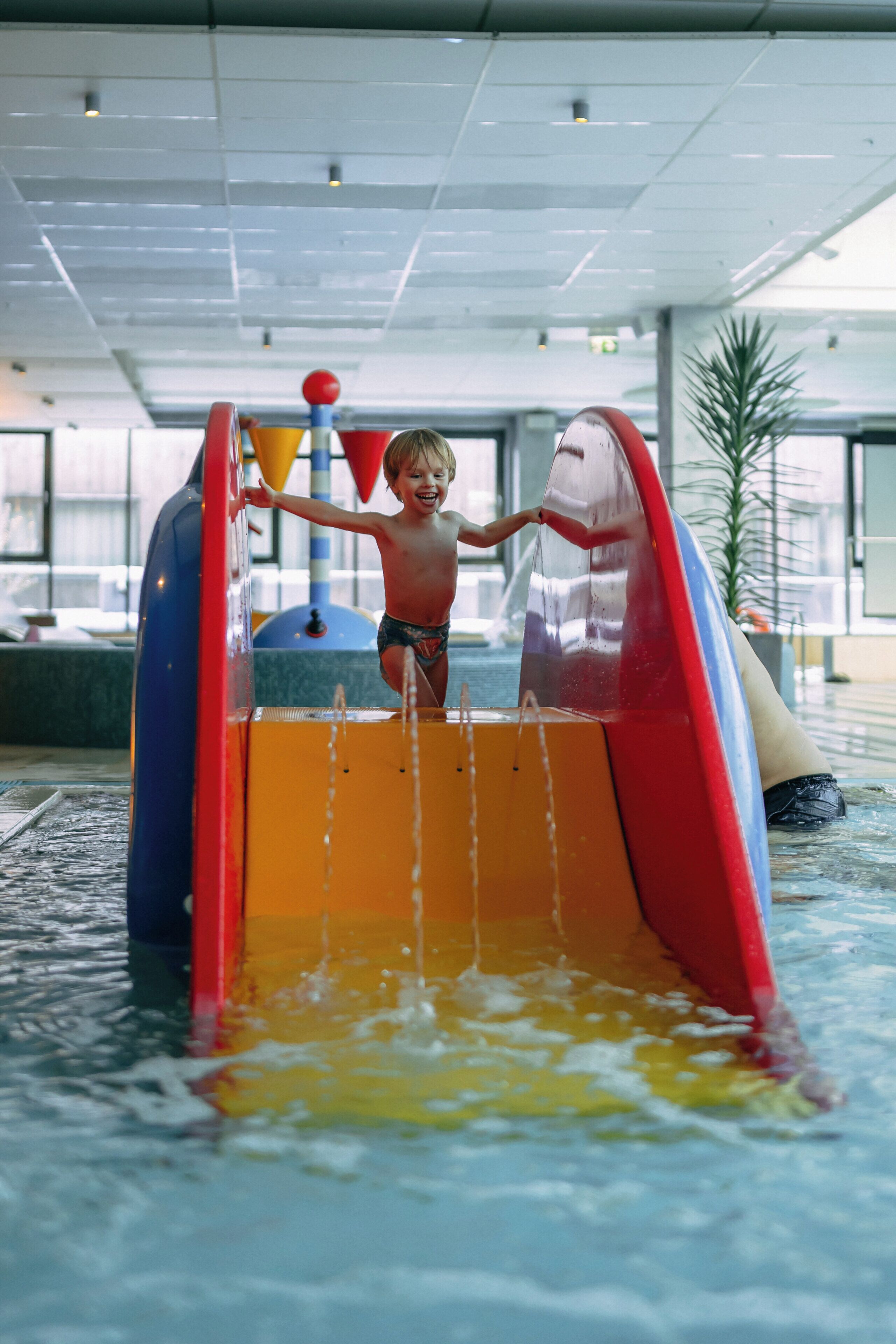 A child playing in a water play area with slides and water jets.