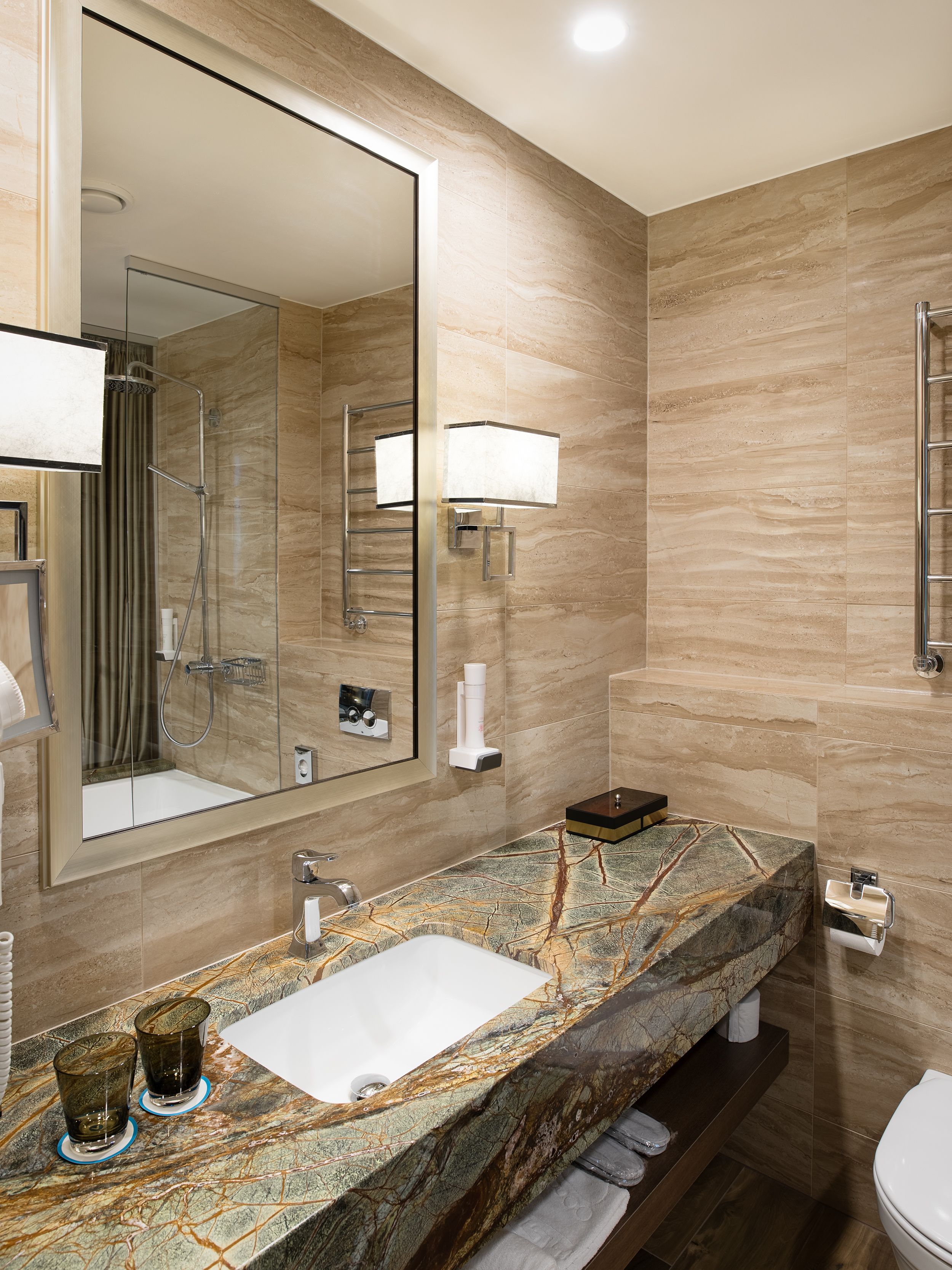 Un baño moderno con lavamanos de mármol, un espejo grande, ducha con mampara de vidrio y un inodoro.